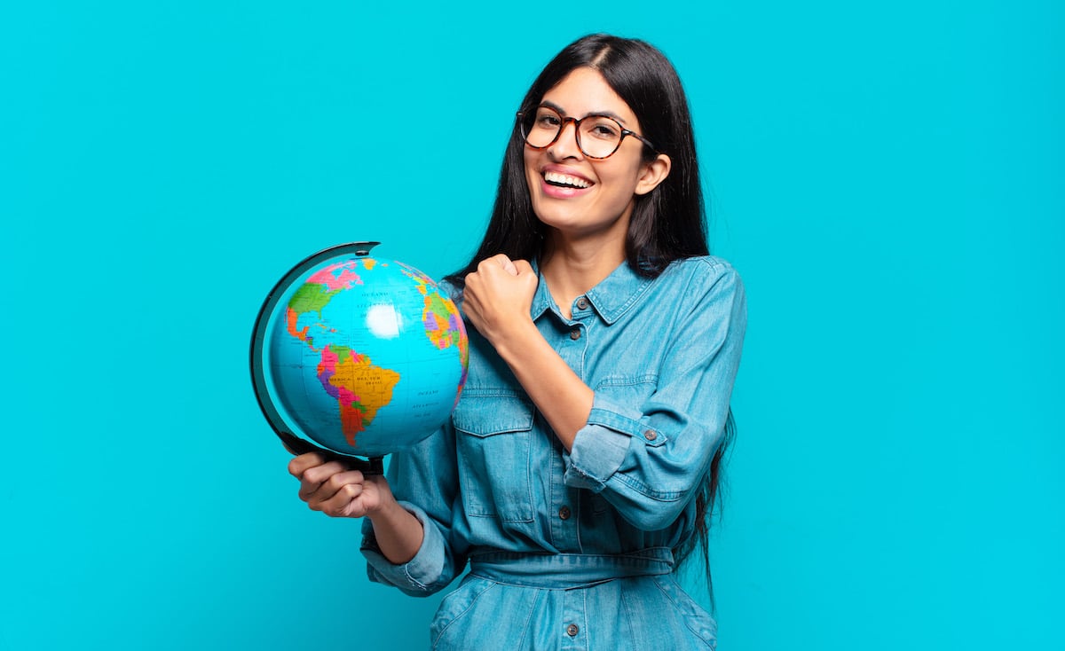 Eine junge Frau hält einen Globus und grinst in die Kamera, weil sie Sprachen gelernt hat und sich damit in anderen Ländern zu verständigen weiß.