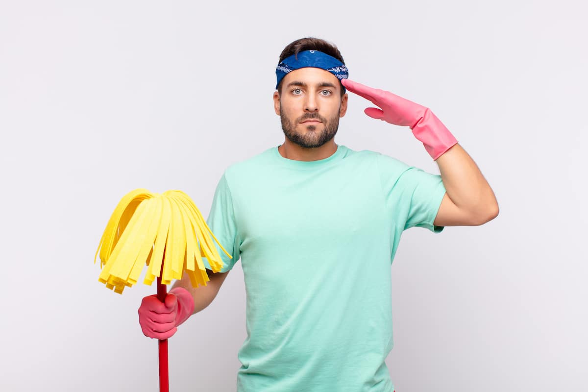 Ein Mann mit Mop und Gummihandschuhen salutiert, weil er dank seinem Putzplan genau weiß, was es zu reinigen gibt.