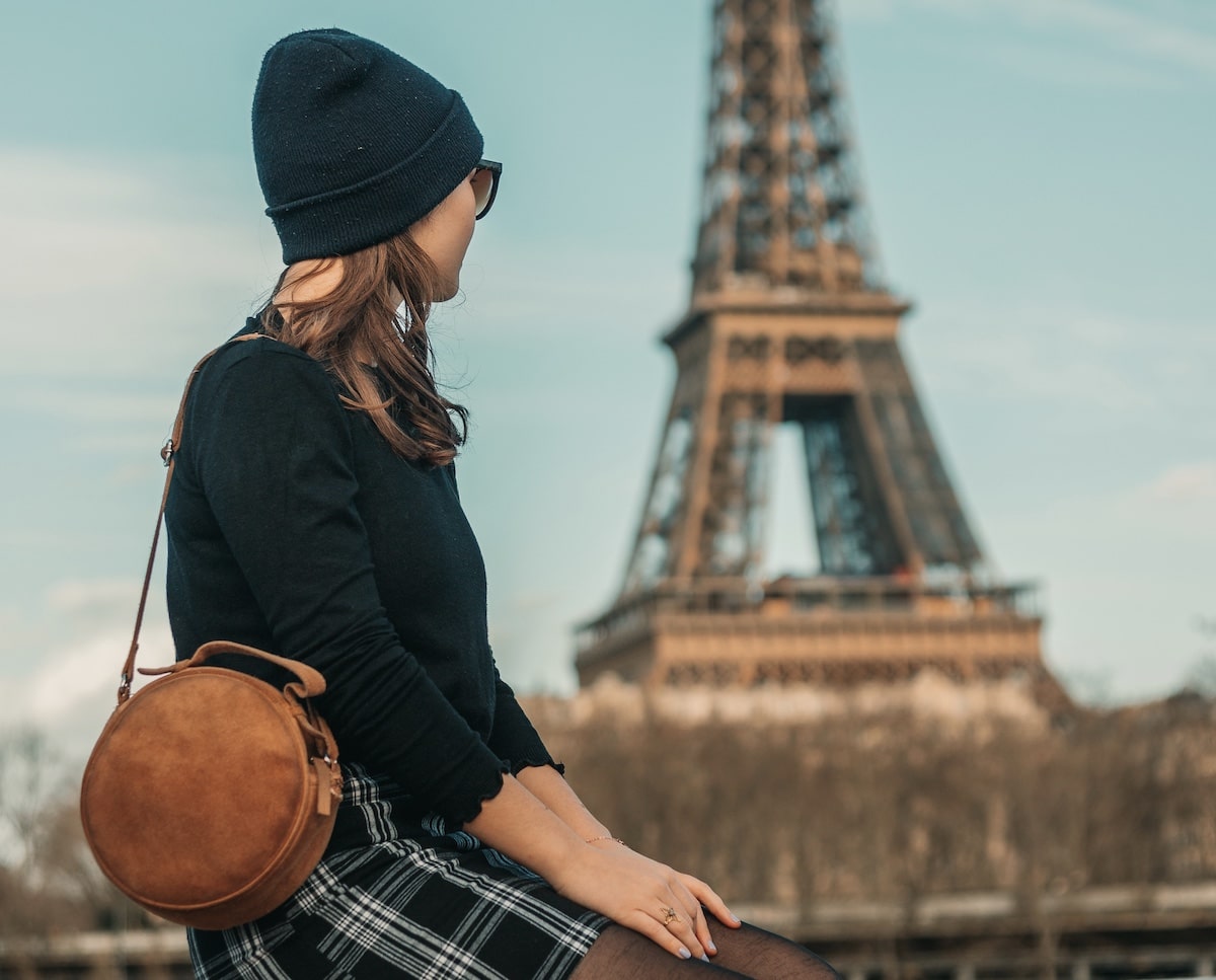 Eine Studentin sitzt bei ihrem Studierenden-Urlaub in Paris vor dem Eiffelturm. Foto von Freitas Junior.