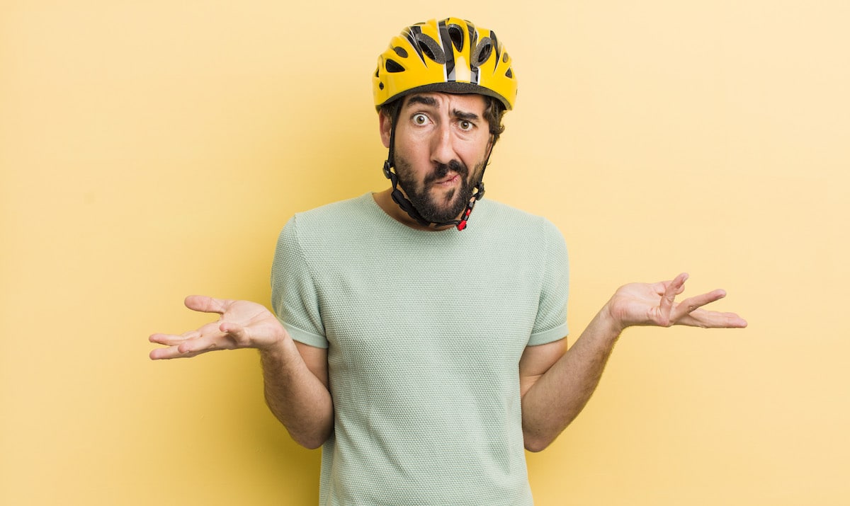 Ein Student mit Helm fragt sich verwundert, was er bei einer Verischerung für das Fahrrad bedenken muss.